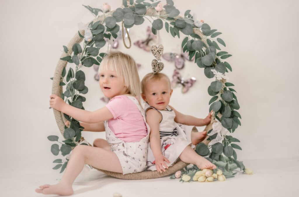 Kleines Mädchen und Kleinkind sitzen in einem Deko Kranz aus Blättern