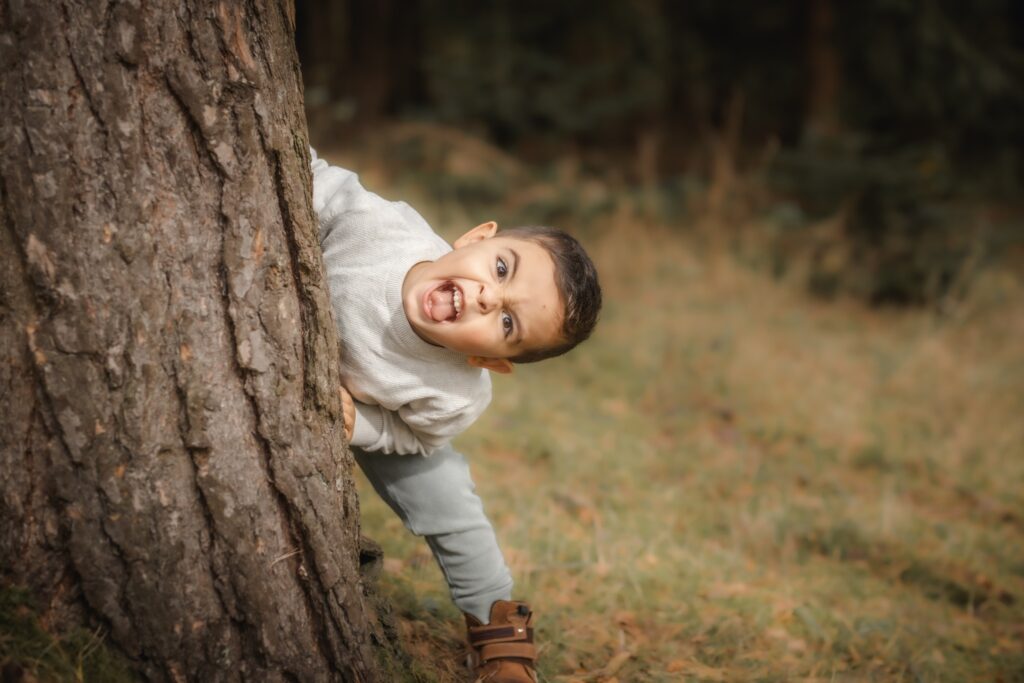 Frecher Junge lehnt hinter Baum und streckt Zunge heraus.